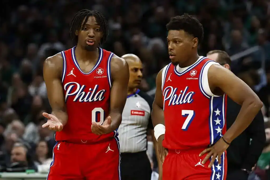 Philadelphia 76ers players in red uniforms talking on the court during an NBA game.