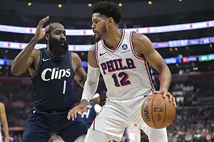 Philadelphia 76ers player in a white jersey drives with the ball while being guarded by a Los Angeles Clippers defender.
