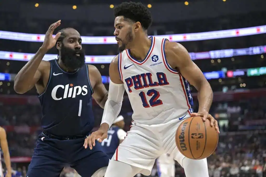 NCAAB 8 Philadelphia 76ers player in a white jersey drives with the ball while being guarded by a Los Angeles Clippers defender.