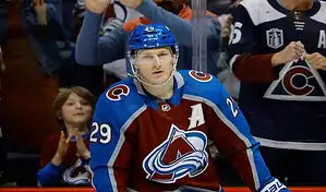 A Colorado Avalanche player in a burgundy uniform with number 29 passing the puck during a game against a Pittsburgh Penguins player in a black uniform with number 71, with a blurred crowd and rink in the background, dated March 24, 2024.