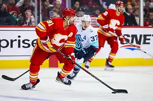Calgary Flames hockey player skating with the puck while a Seattle Kraken player chases.