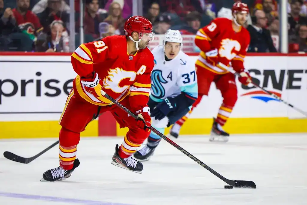 Calgary Flames hockey player skating with the puck while a Seattle Kraken player chases.