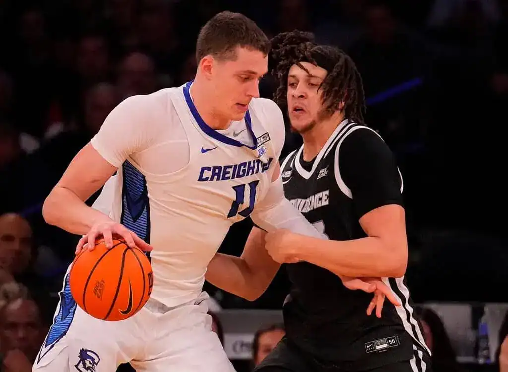 A basketball player in a Creighton uniform dribbles while closely guarded by an opponent in a Providence uniform, showcasing intense action.