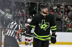 Dallas Stars hockey player wearing a black jersey with neon green accents, holding his stick during NHL action.