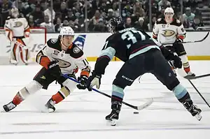 A dynamic moment in an ice hockey game with players from opposing teams competing for the puck on the rink, surrounded by spectators.