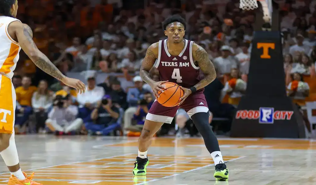 Texas A&M Aggies player dribbles the ball while being guarded by a Georgia Bulldogs defender during a college basketball game.