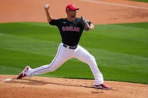 Cleveland Guardians pitcher in mid-throw during a baseball game, wearing the team’s black jersey and white pants.