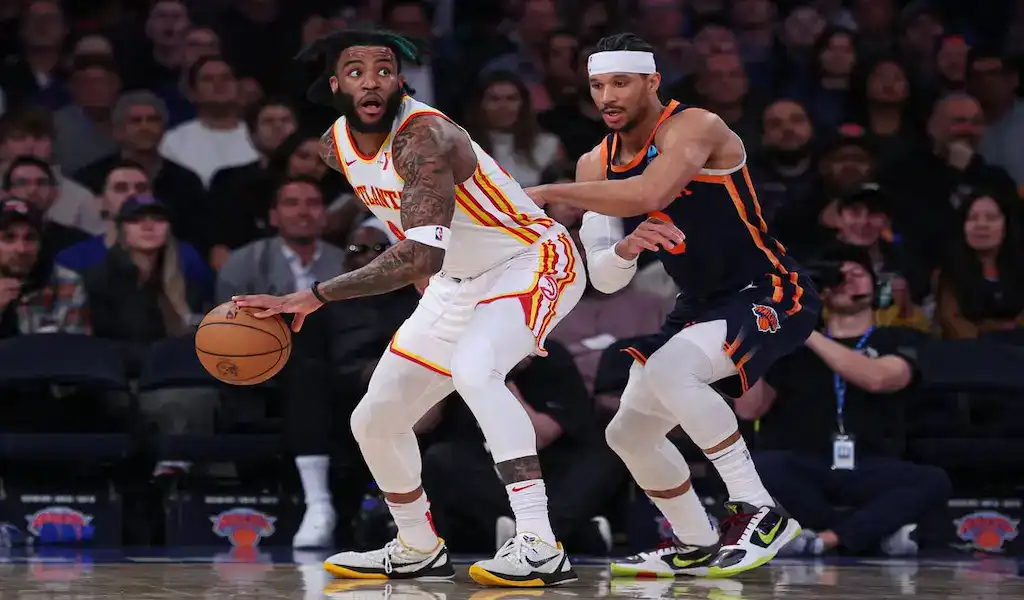 Atlanta Hawks player holds the ball under pressure from a New York Knicks defender during an NBA game.