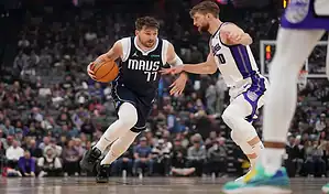 Dallas Mavericks player drives to the basket while defended by a Sacramento Kings player during an NBA game.