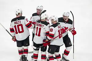 New Jersey Devils players in white jerseys gather and celebrate on the ice.