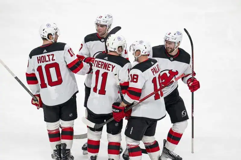 New Jersey Devils players in white jerseys gather and celebrate on the ice.