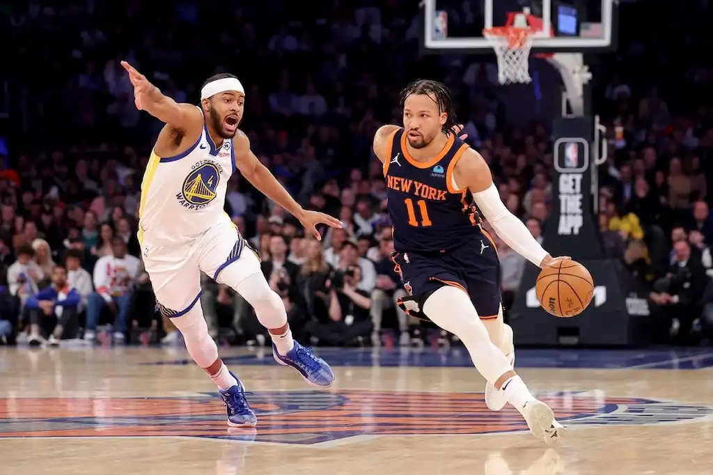 6 NY Knicks player dribbles the basketball up the court while being closely defended by a GS Warriors player.