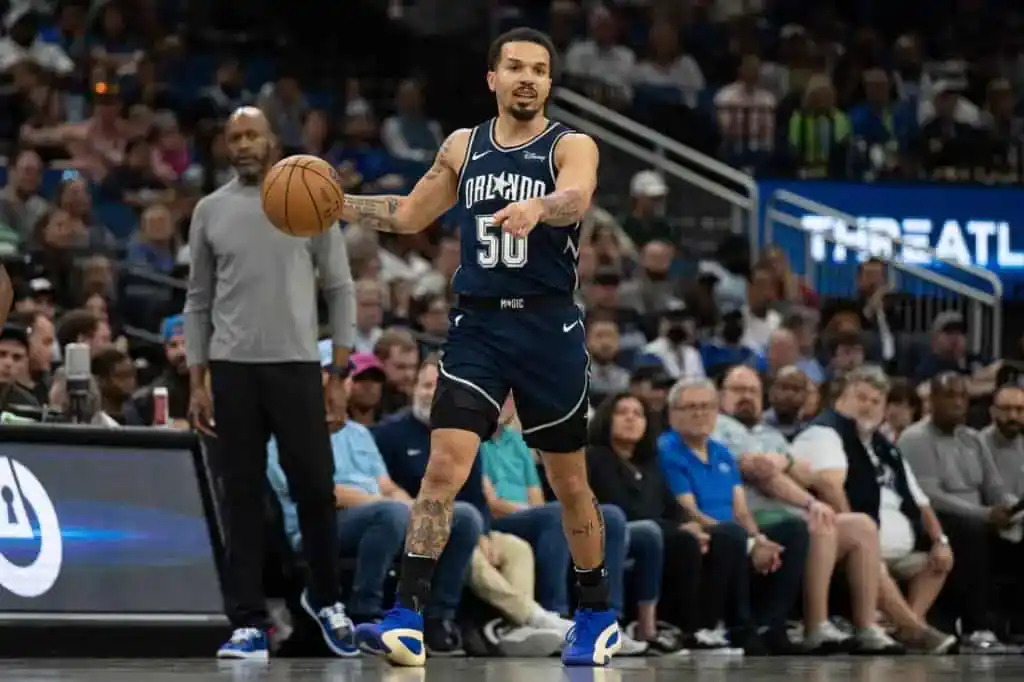 2 Orlando Magic player wearing number 50 dribbling the ball at midcourt while surveying the play during an NBA game.