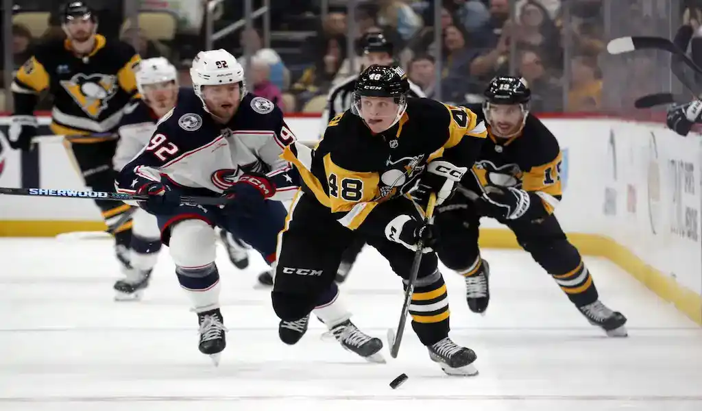 Pittsburgh Penguins and Columbus Blue Jackets players compete during a fast-paced hockey game on the ice.