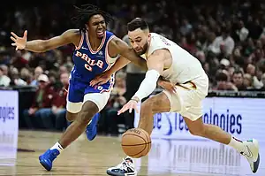 A tense moment in a basketball game, with two players competing for the ball, showcasing dynamic movement on the court.