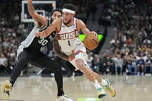 Phoenix Suns player in a white jersey drives past a San Antonio Spurs defender while dribbling the basketball.