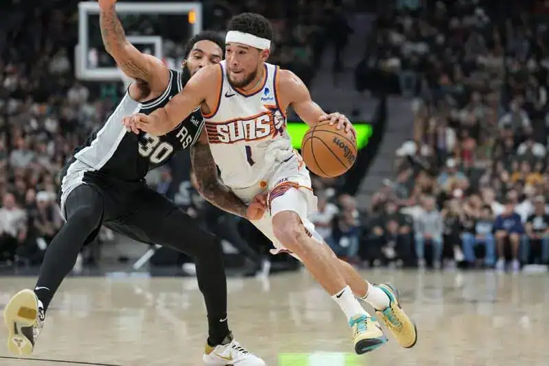 Phoenix Suns player in a white jersey drives past a San Antonio Spurs defender while dribbling the basketball.