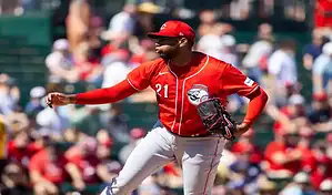 Cincinnati Reds pitcher in red uniform winds up to throw a pitch during a game against the Washington Nationals.