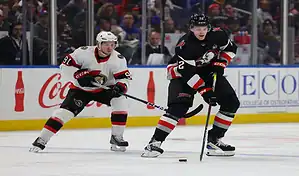Buffalo Sabres player skating with the puck against Ottawa Senators defender during an NHL matchup.