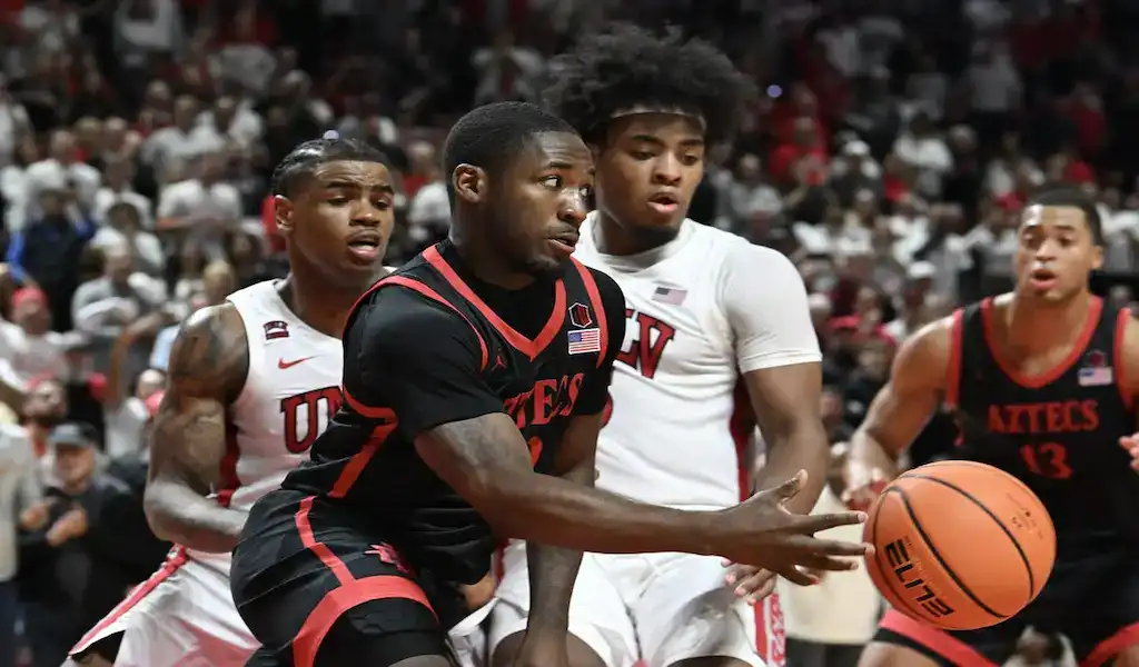 NCAAB 6 San Diego State Aztecs player drives to the basket against UNLV defenders during a college basketball game.