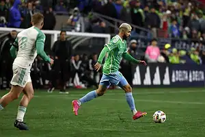 Seattle Sounders soccer player dribbles the ball during a match while a defender closes in.