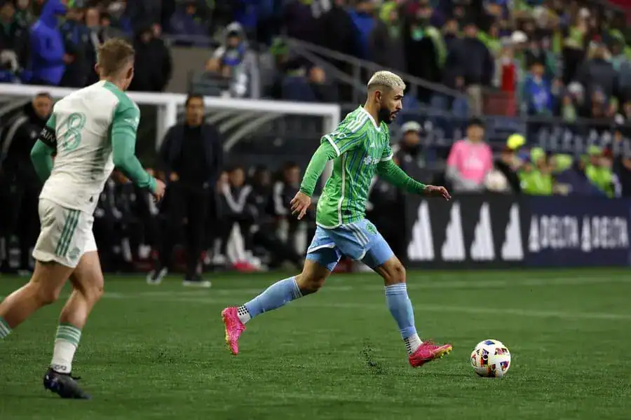 Seattle Sounders soccer player dribbles the ball during a match while a defender closes in.