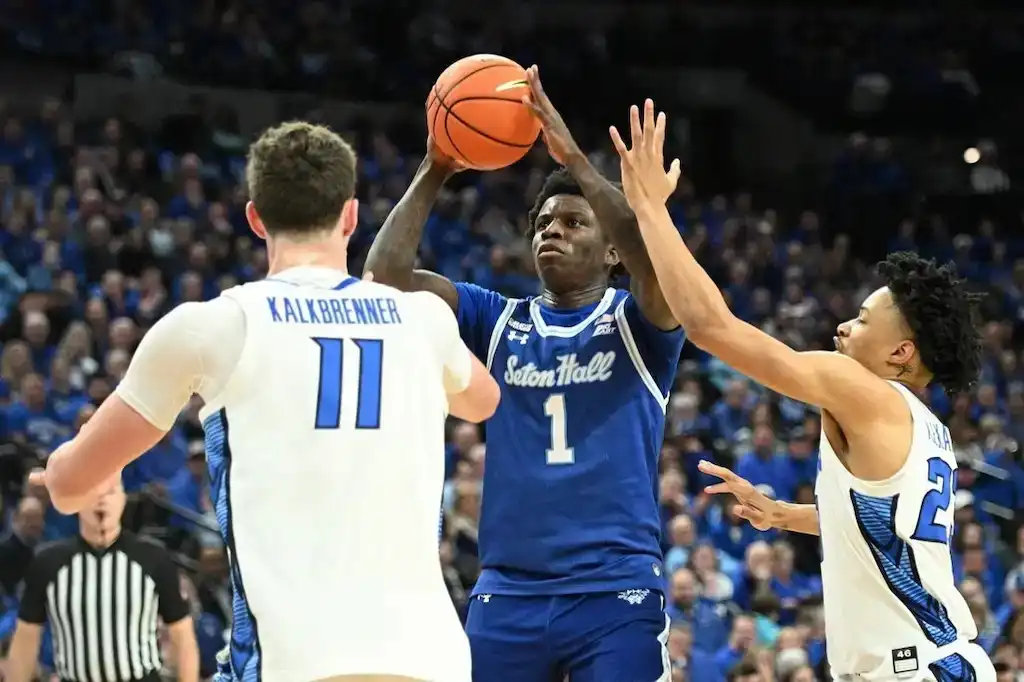 Seton Hall player attempts a jump shot while being defended by two players.