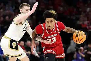 Wisconsin Badgers guard dribbles past a Purdue defender, showing speed and control during an NCAA college basketball game
