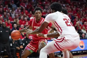 A Wisconsin basketball player looks to make a play while being tightly defended by two players.