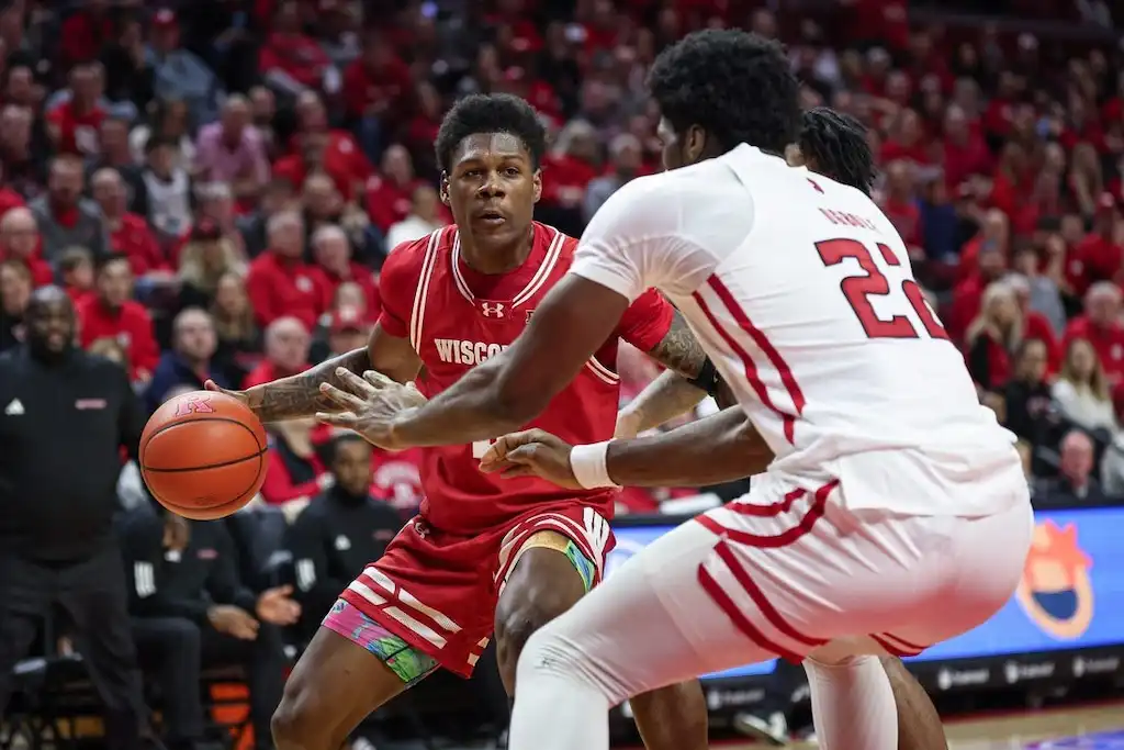 A Wisconsin basketball player looks to make a play while being tightly defended by two players.