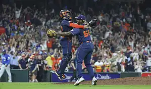 Houston Astros catcher and pitcher celebrate a win on the field as fans cheer in the background during an MLB game.