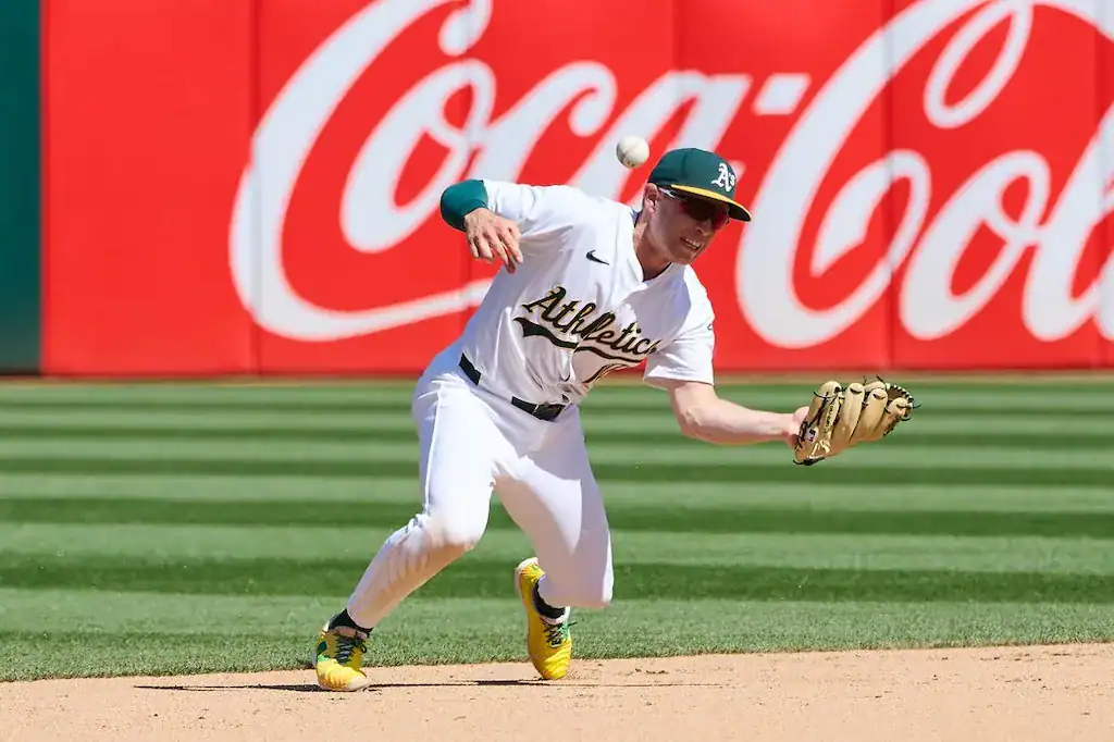 7 A baseball player in a white Athletics uniform fields a ball, with a vibrant Coca-Cola advertisement in the background.