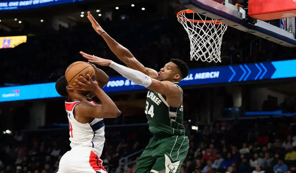 Milwaukee Bucks player contests a shot by a Washington Wizards player under the basket during an NBA game.