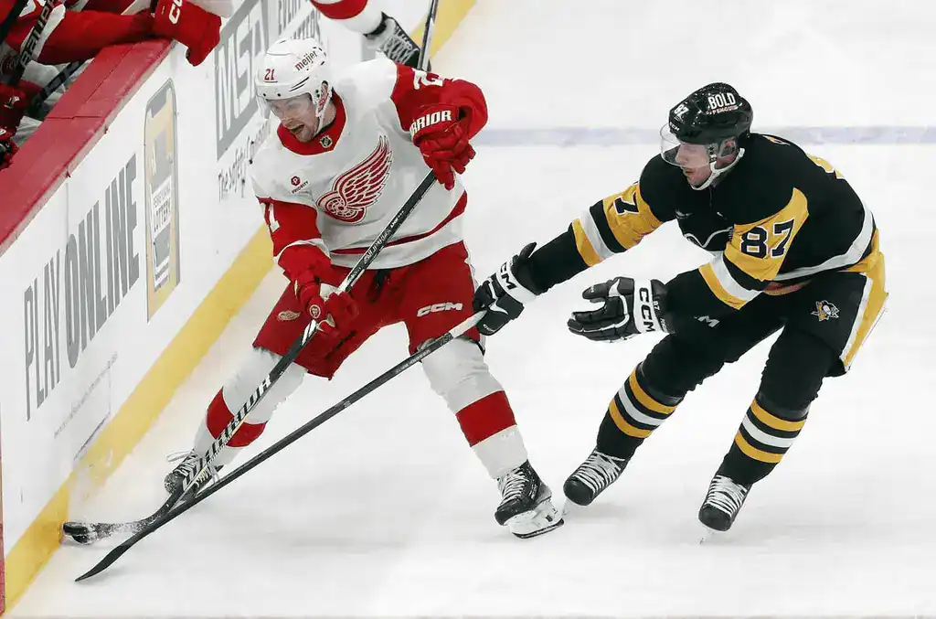 Detroit Red Wings player controls puck against Penguins defender.