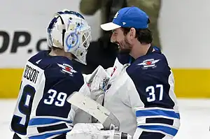 Winnipeg Jets goalie in full pads smiles while talking with a teammate after a game.