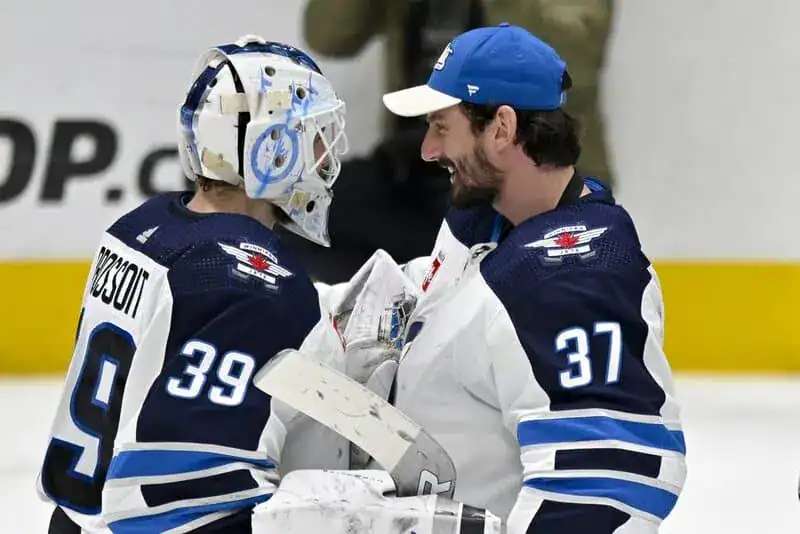 Winnipeg Jets goalie in full pads smiles while talking with a teammate after a game.