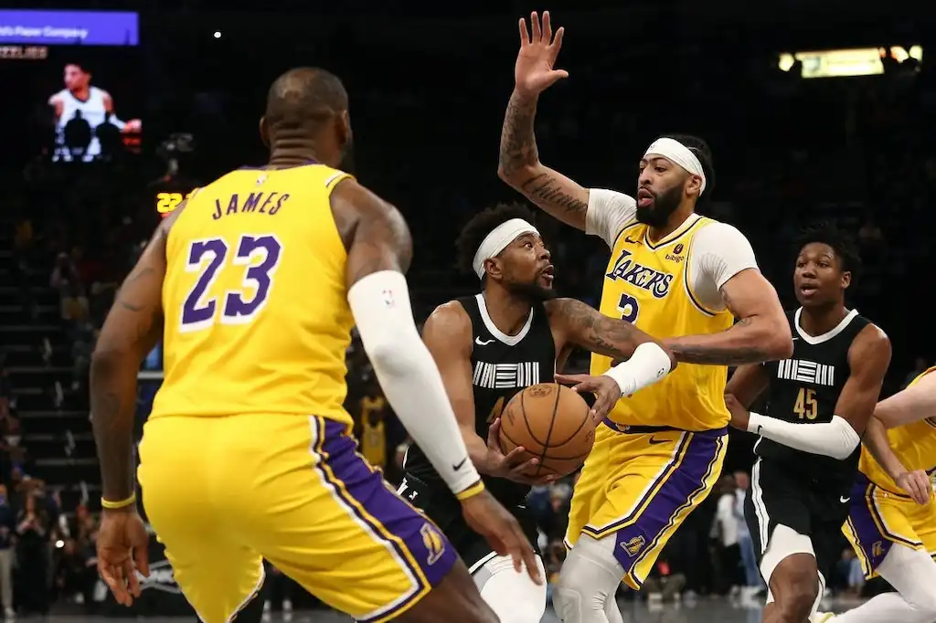 A Lakers player raises his arm to defend as an opposing player drives to the basket.