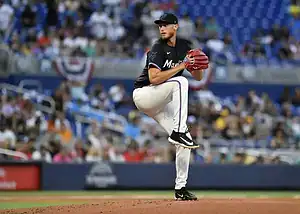 A baseball player from the Miami Marlins executing a windup pitch on the mound, with a blurred crowd in the background.