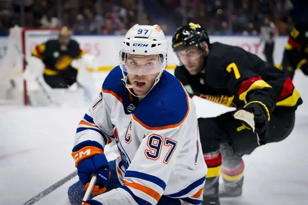 An intense hockey match scene with players in team jerseys, one maneuvering the puck while an opponent trails closely behind.