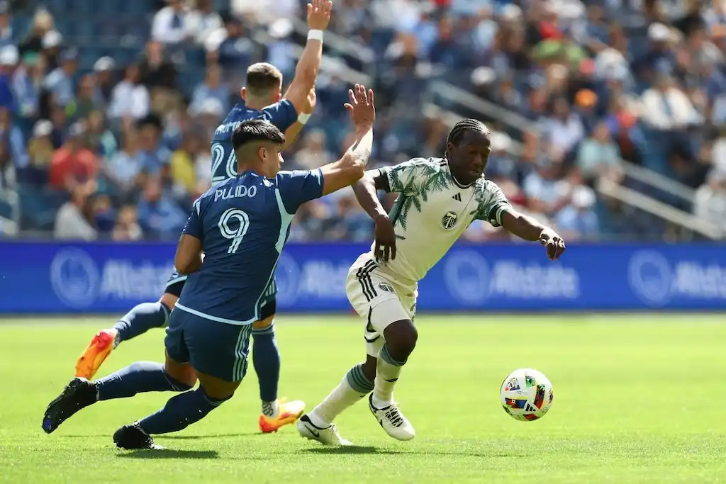 A Portland Timbers soccer player dribbles the ball past a defender.