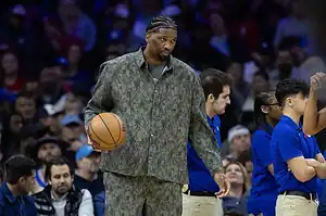 NBA player holding a basketball courtside in casual clothing.