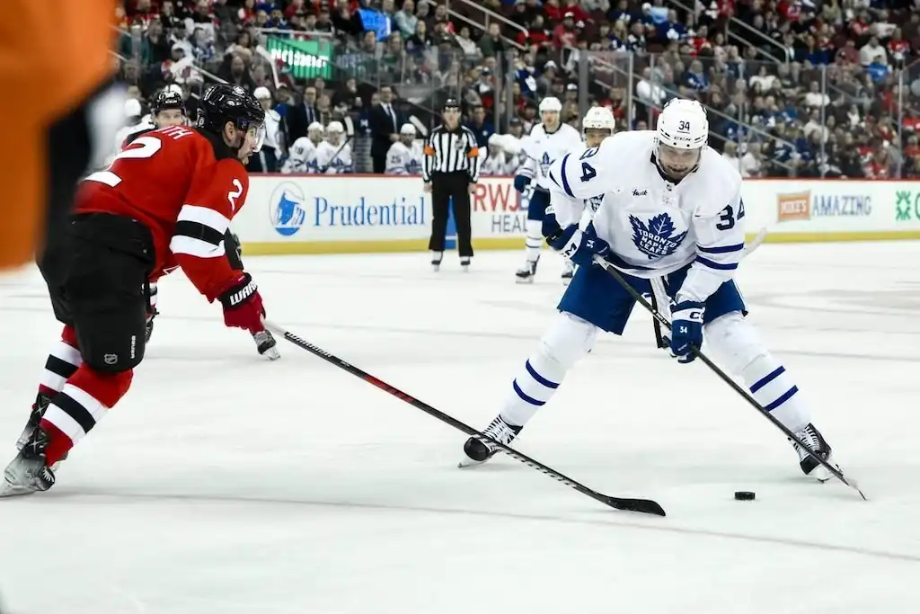 NHL 7 A Toronto Maple Leafs player controls the puck while being defended by a New Jersey Devils player.