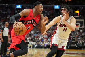 A Toronto Raptors player drives to the basket while being closely guarded by a Miami Heat defender.