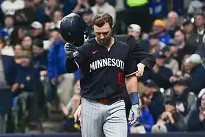 Minnesota Twins baseball player in a black jersey removes his helmet while walking off the field.
