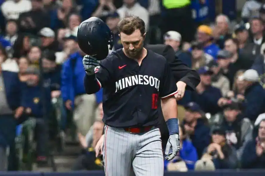 3 Minnesota Twins baseball player in a black jersey removes his helmet while walking off the field.