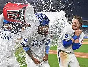 Two Royals players are soaked in a postgame celebration as a teammate pours water from a cooler over them.