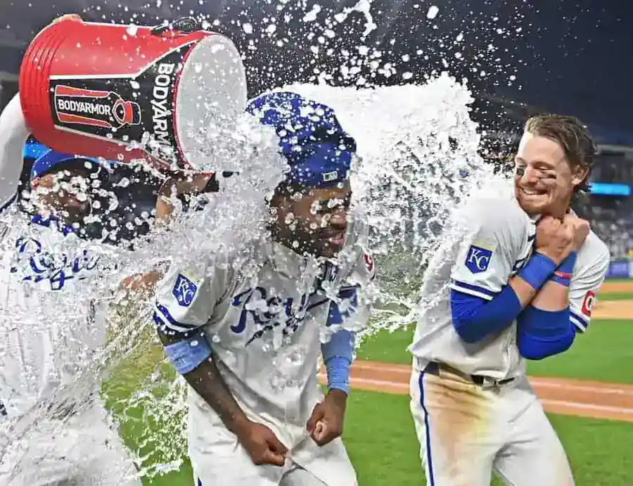 Two Royals players are soaked in a postgame celebration as a teammate pours water from a cooler over them.