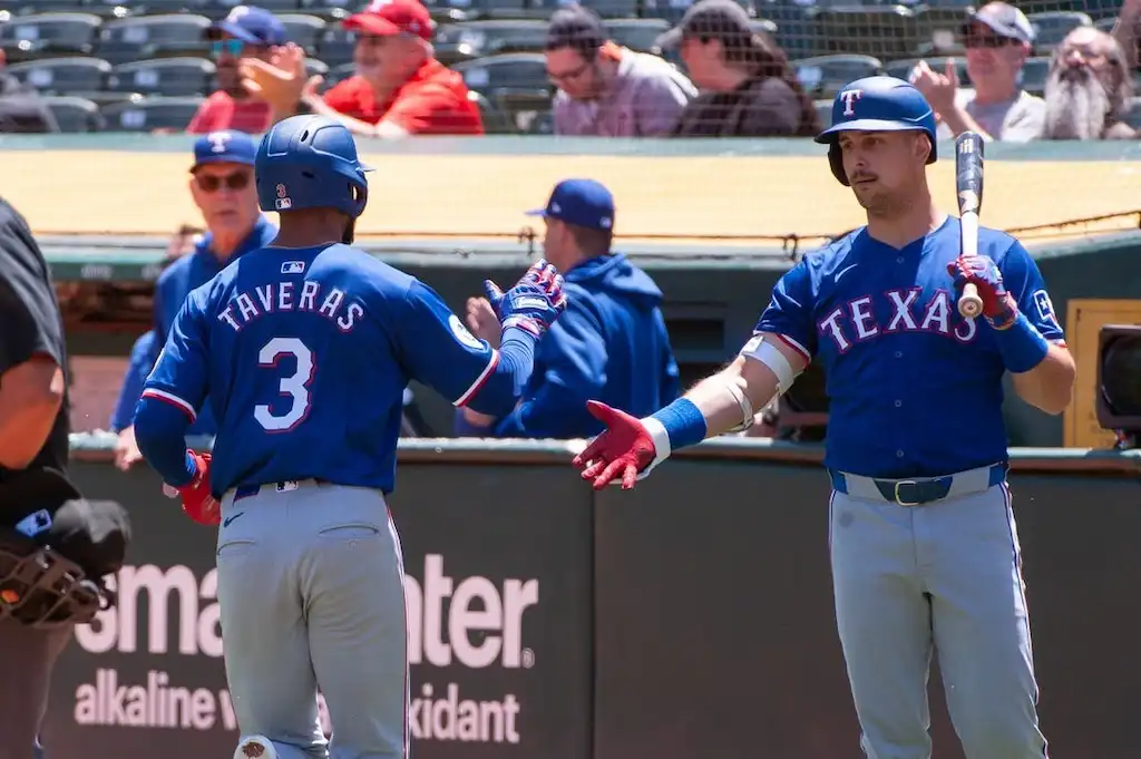 6 Texas Rangers baseball players exchange a fist bump near the dugout.