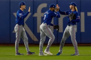 Three Texas Rangers players celebrate in the outfield with high-fives after a successful play.