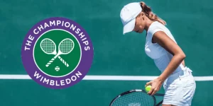 A tennis player in a white outfit prepares to serve on a green court, with the Wimbledon Championships logo in the corner.